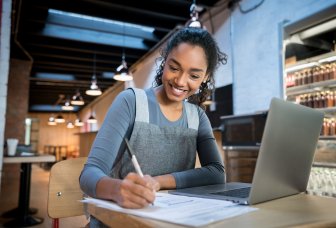 foto dame som sitter på restaurant mens hun jobber på pc og noterer på ark
