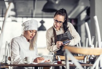 Kvinnelig kokk og servitør med ipad og kalkulator. Foto